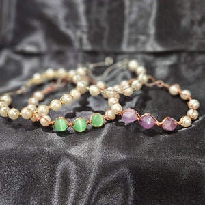 Può includere: Tre braccialetti con perle bianche, pietre preziose verdi e viola e filo di rame.