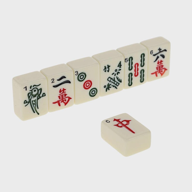 May include: A set of ivory-colored Mahjong tiles with black, red, and green symbols. The tiles are arranged in a row, with one tile separate. The symbols include numbers, circles, and Chinese characters.