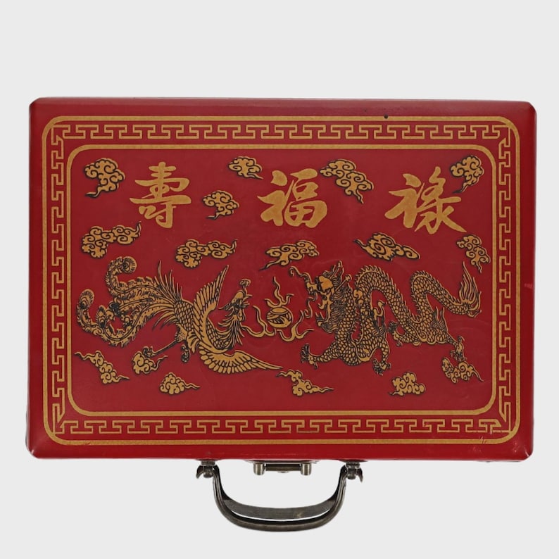 May include: A red rectangular box with a gold border and handle. The box features gold illustrations of a phoenix and a dragon, along with Chinese characters and cloud motifs. The overall design is ornate and traditional.