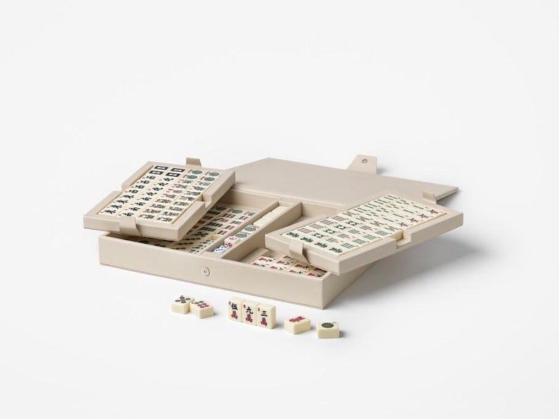 Puede incluir: Un juego de Mahjong beige con fichas y una caja de almacenamiento. La caja est&aacute; abierta, revelando m&uacute;ltiples bandejas de fichas con s&iacute;mbolos negros y rojos. Varias fichas sueltas est&aacute;n esparcidas frente a la caja.