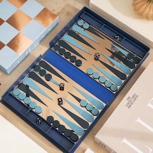 May include: Backgammon set with a blue and gold colour scheme. The board is open, showing the playing surface with dice and game pieces. A box labelled "CHESS" is visible in the background.