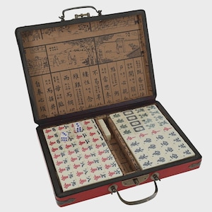 May include: A red Mahjong set in a black case, open to reveal tiles, dice, and other game components. The case has a handle and a decorative interior with Chinese characters and illustrations. The tiles are white with red and blue markings.