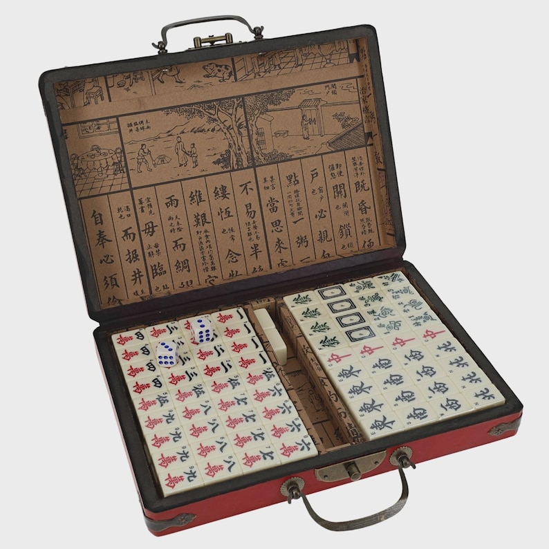 May include: A red Mahjong set in a black case, open to reveal tiles, dice, and other game components. The case has a handle and a decorative interior with Chinese characters and illustrations. The tiles are white with red and blue markings.