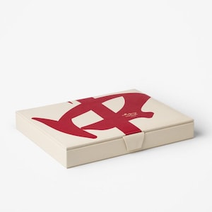 Puede incluir: Caja rectangular blanquecina con un gran dise&ntilde;o abstracto rojo en la tapa. La caja tiene un peque&ntilde;o cierre de broche. El texto "Maligry" est&aacute; impreso en la tapa. Un elemento gr&aacute;fico llamativo.