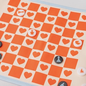 May include: A foldable chess board with an orange and cream heart-patterned design. The board has a light blue border and includes black and white chess pieces. The board is open and ready for play.
