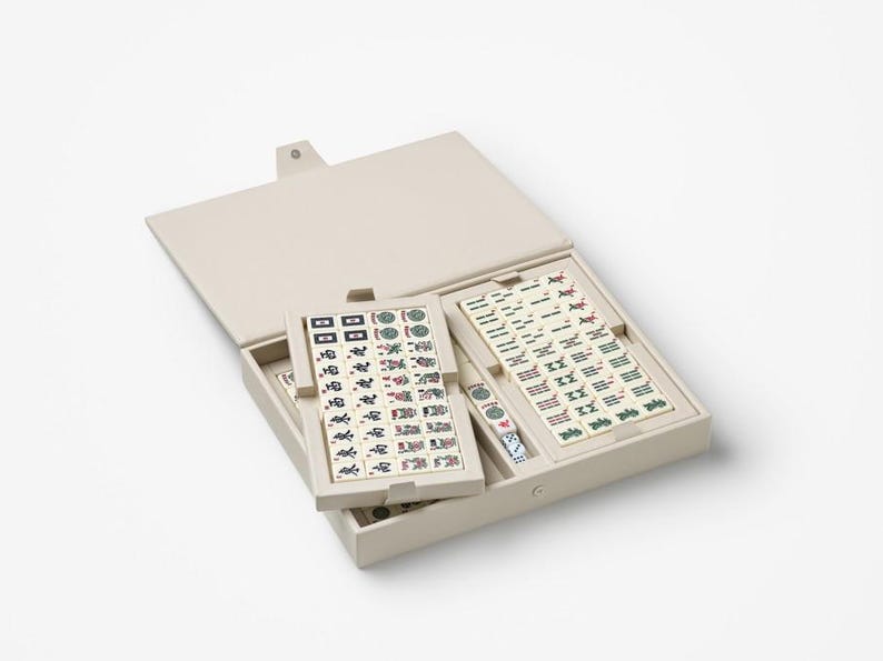 Puede incluir: Un juego de Mahjong beige con fichas dispuestas dentro de un estuche a juego. El estuche est&aacute; abierto, revelando las fichas con varios s&iacute;mbolos y caracteres. El juego incluye dados y est&aacute; dise&ntilde;ado para el cl&aacute;sico juego de fichas.