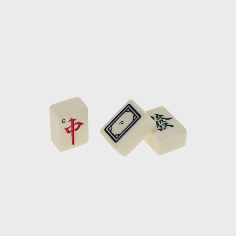 May include: Three off-white Mahjong tiles with black, red, and green symbols. One tile has a red Chinese character, another has a black rectangle, and the third has a green Chinese character. The tiles are arranged on a light gray background.