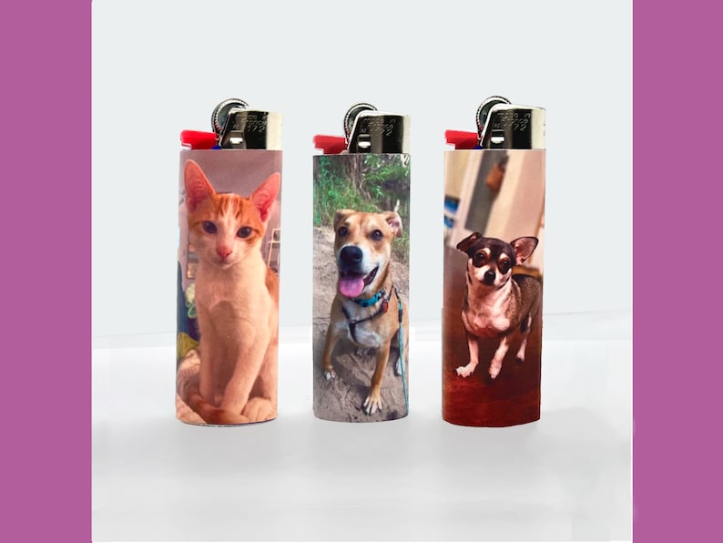 Puede incluir: Tres encendedores con im&aacute;genes personalizadas de mascotas. Uno presenta un gato naranja y blanco, otro un perro marr&oacute;n con un collar azul y el tercero un perro marr&oacute;n y negro. Cada encendedor tiene un bot&oacute;n de encendido rojo y una parte superior de metal plateado.