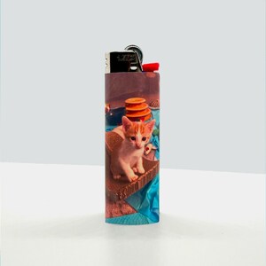 Puede incluir: Un encendedor con un dise&ntilde;o colorido que presenta un gatito sentado en una superficie azul y marr&oacute;n. El gatito tiene pelaje blanco con marcas naranjas.