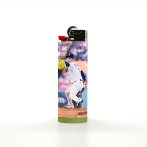 May include: A rectangular lighter featuring a baseball player in a white and blue uniform, with a yellow glove, in action on a baseball field. The lighter has a black top with a red ignition button and a green base.