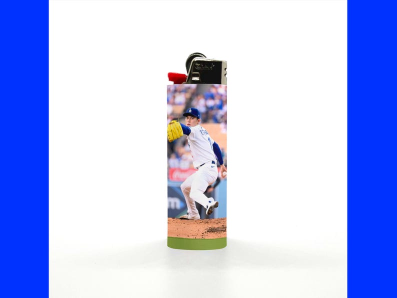 May include: A rectangular lighter featuring a baseball player in a white and blue uniform, with a yellow glove, in action on a baseball field. The lighter has a black top with a red ignition button and a green base.