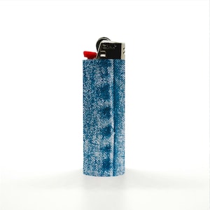 May include: A blue denim-patterned lighter with a red ignition button. The lighter is set against a white background, with vertical denim fabric strips on either side. The lighter's metal top contrasts with the denim design.