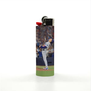 May include: A black and silver lighter with a baseball player image. The lighter features a red ignition button and a detailed image of a baseball player in action. The background shows a stadium filled with spectators.