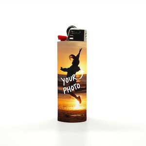 Puede incluir: Un encendedor personalizado con la parte superior negra y un bot&oacute;n de encendido rojo. El cuerpo presenta una silueta de una persona saltando al atardecer, con el texto "YOUR PHOTO" en blanco.