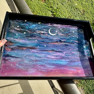 Könnte beinhalten: Schwarzes rechteckiges Serviertablett mit einem Himmelsdesign. Die Oberfläche des Tabletts zeigt eine lebendige Malerei eines Nachthimmels mit einem Mond, Sternen und wirbelnden Wolken in Blau-, Lila- und Rosatönen.
