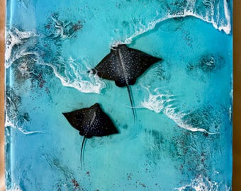 May include: A rectangular resin art piece featuring two black spotted stingrays swimming in turquoise and blue ocean water. The surface displays textured white foam waves and deep blue depths, creating a three-dimensional effect of the sea.