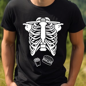 May include: Black t-shirt with a white graphic of a rib cage, a hamburger, and french fries. The shirt is made of a soft material and is suitable for casual wear. The design is simple and eye-catching.