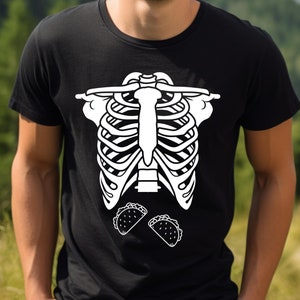 May include: Black t-shirt featuring a white skeleton rib cage design with two tacos below. The shirt is made of a soft material and is suitable for casual wear. The design is a fun and unique graphic.