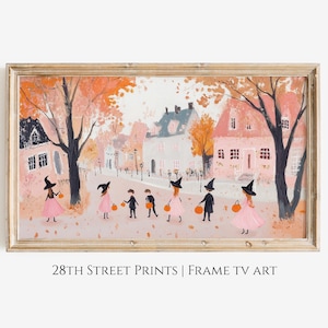 May include: A vintage-style illustration of children dressed as witches trick-or-treating in a small town. The children are wearing pink dresses and black witch hats. The houses are painted in pastel colors and the trees are orange and yellow, suggesting autumn. The image is framed in a light wood frame.