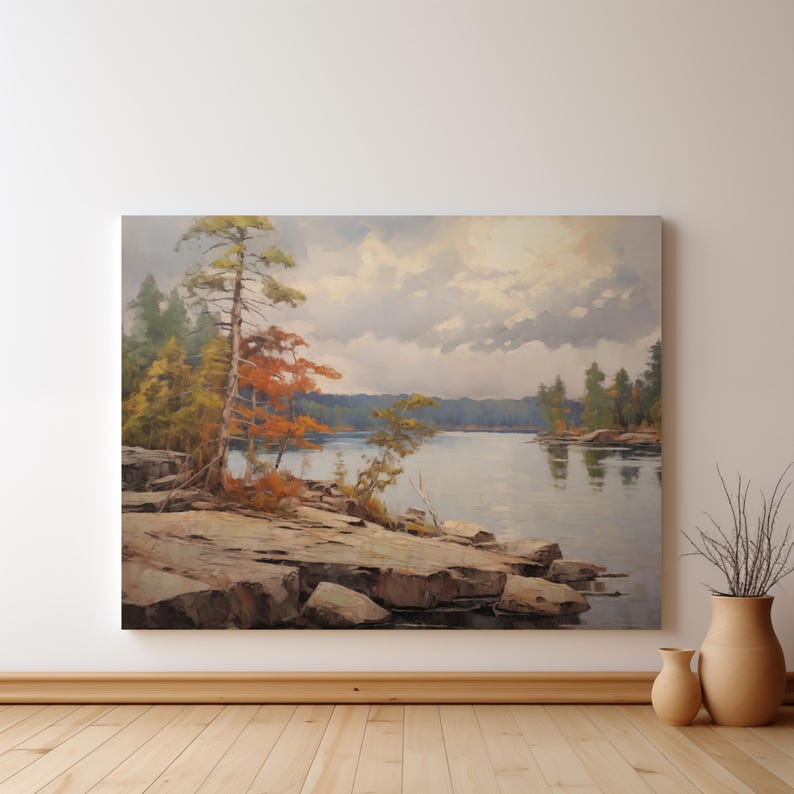 May include: A painting of a lake scene with a rocky shoreline and trees. The sky is cloudy and the water is calm. The trees are mostly green, but there are some red and orange leaves on the trees in the foreground.