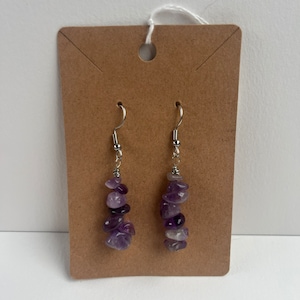 Könnte beinhalten: Ein Paar Ohrringe mit einem silbernen Haken und einem Cluster aus Amethyststeinen in verschiedenen Violetttönen.
