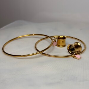 May include: Two gold hoop earrings with a gold ear gauge with pink heart charms.