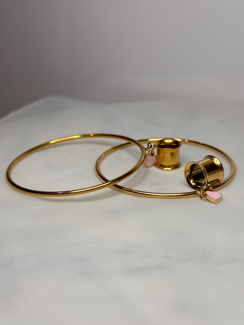May include: Two gold hoop earrings with a gold ear gauge with pink heart charms.