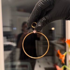 May include: A gold hoop earring with a small pink heart charm hanging from it.
