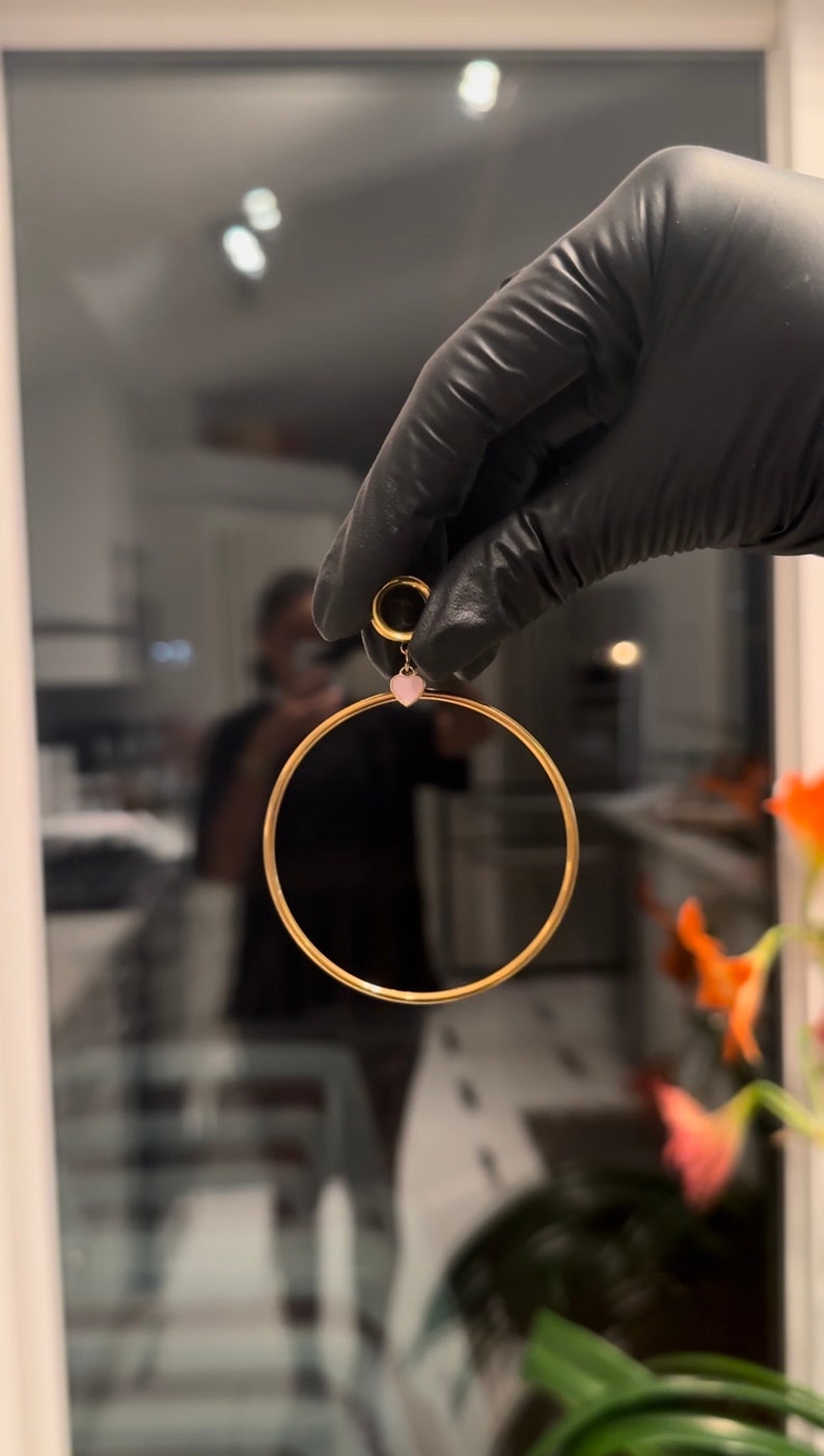May include: A gold hoop earring with a small pink heart charm hanging from it.