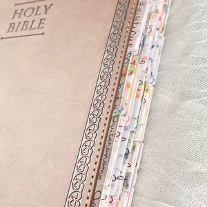 Puede incluir: Una Biblia encuadernada en cuero marr&oacute;n con un borde decorativo en relieve y separadores de p&aacute;gina con estampado floral.