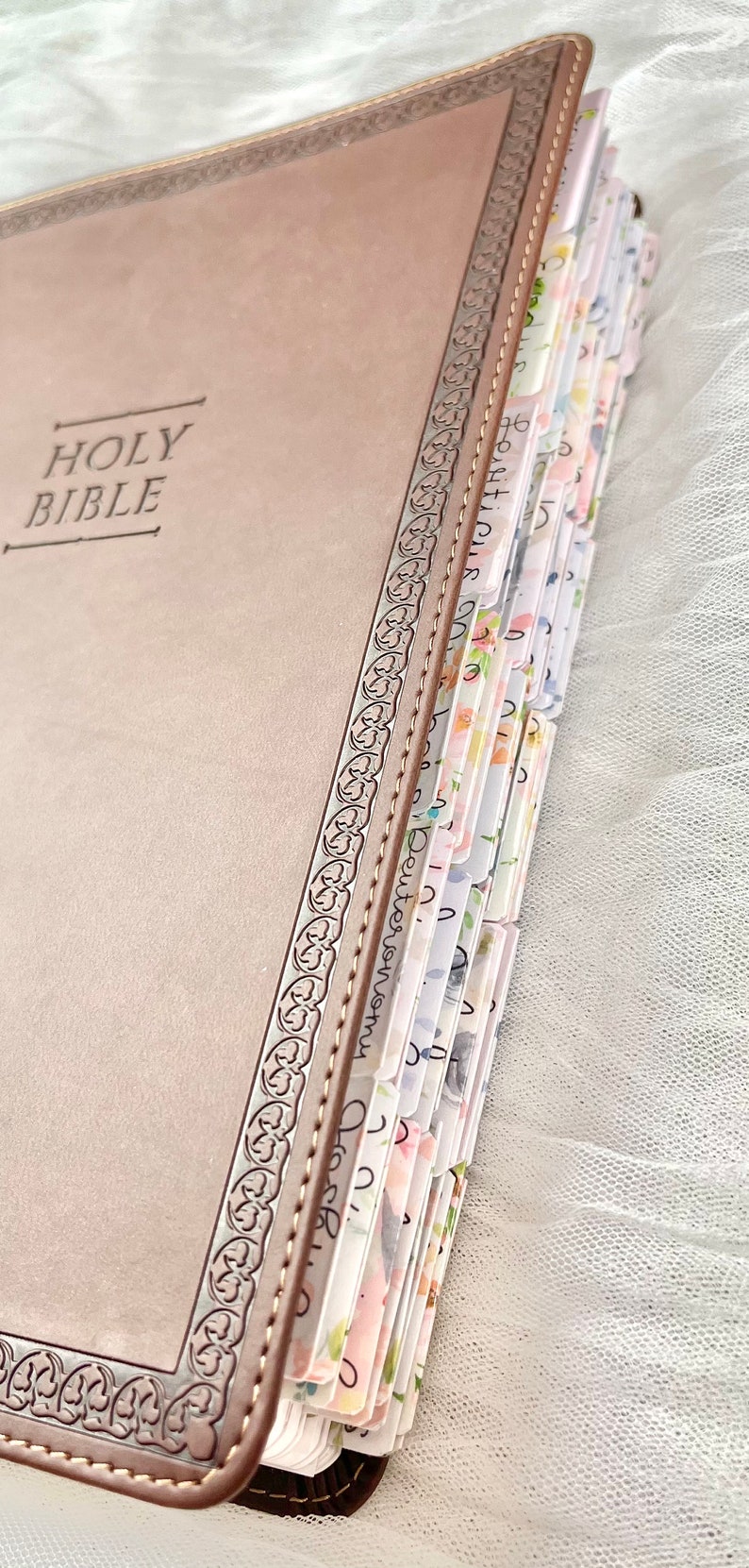 Puede incluir: Una Biblia encuadernada en cuero marr&oacute;n con un borde decorativo en relieve y separadores de p&aacute;gina con estampado floral.