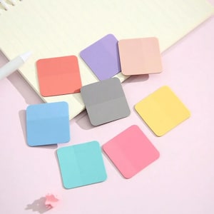 May include: Eight square sticky notes in various pastel colors, including pink, blue, yellow, gray, and green. The notes are arranged on a pink surface.