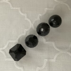 Peut inclure: Cinq perles en verre noir, quatre rondes et une carrée, avec un design facetté.
