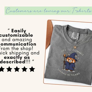 Może przedstawiać: Szara koszulka z napisem "Off to Commit" i kresk&oacute;wkową czerwoną pandą w czapce i szacie czarodzieja. Pod grafiką znajduje się napis "Shenau Actigans". Na koszulce jest złoty naszyjnik.