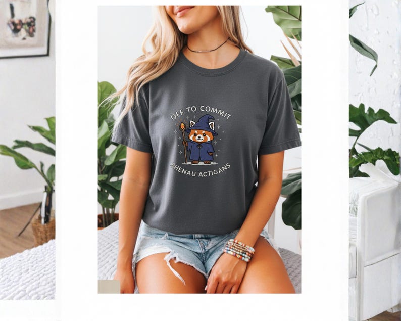 Może przedstawiać: Ciemnoszara koszulka z napisem "OFF TO COMMIT SHENAU ACTIGANS" i kresk&oacute;wkową czerwoną pandą w czapce i szacie czarodzieja. Panda trzyma laskę. Koszulka jest z kr&oacute;tkim rękawem.