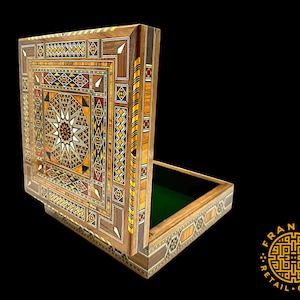 May include: A wooden box with intricate inlaid designs in various shades of brown, red, and yellow. The box is open, revealing a green felt lining inside. The box is decorated with a star-shaped pattern in the center.