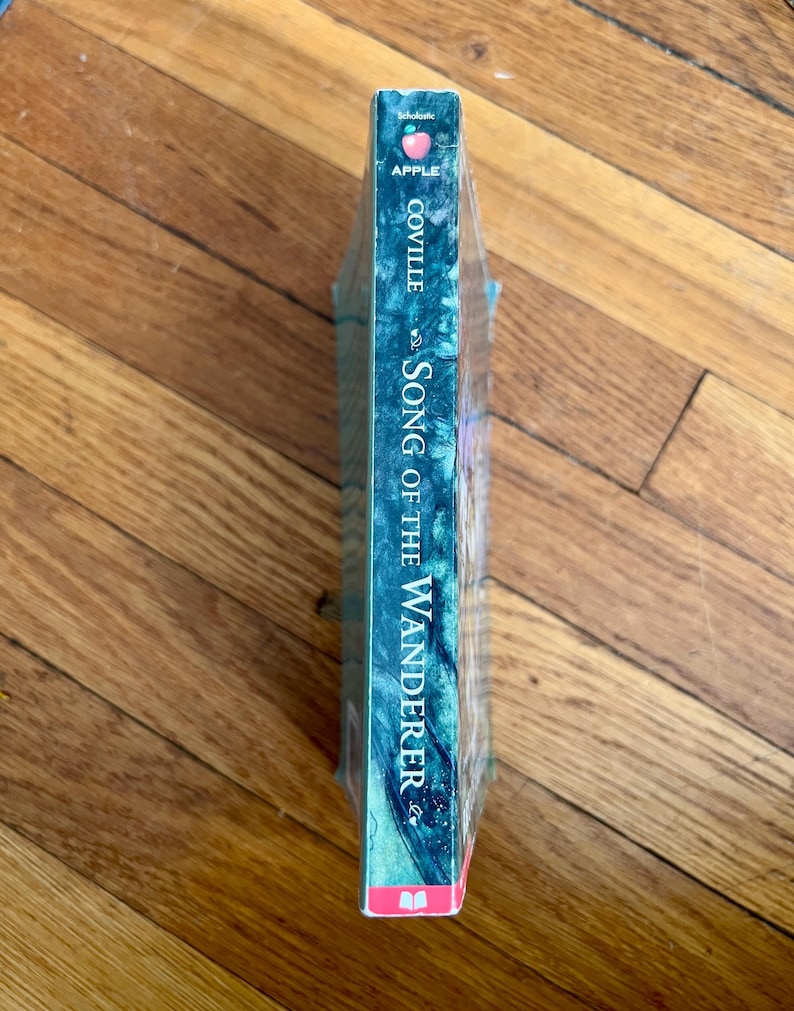 May include: A paperback book titled "Song of the Wanderer" by Coville. The book has a teal and blue cover with the word "Apple" and a pink apple logo at the top. The book is wrapped in clear plastic.