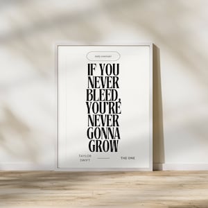 以下が含まれることがあります： 「IF YOU NEVER BLEED, YOU'RE NEVER GONNA GROW」の黒いテキストが書かれた、Taylor Swiftによる額入りのプリント。プリントは白い背景で、木製の床に展示されています。