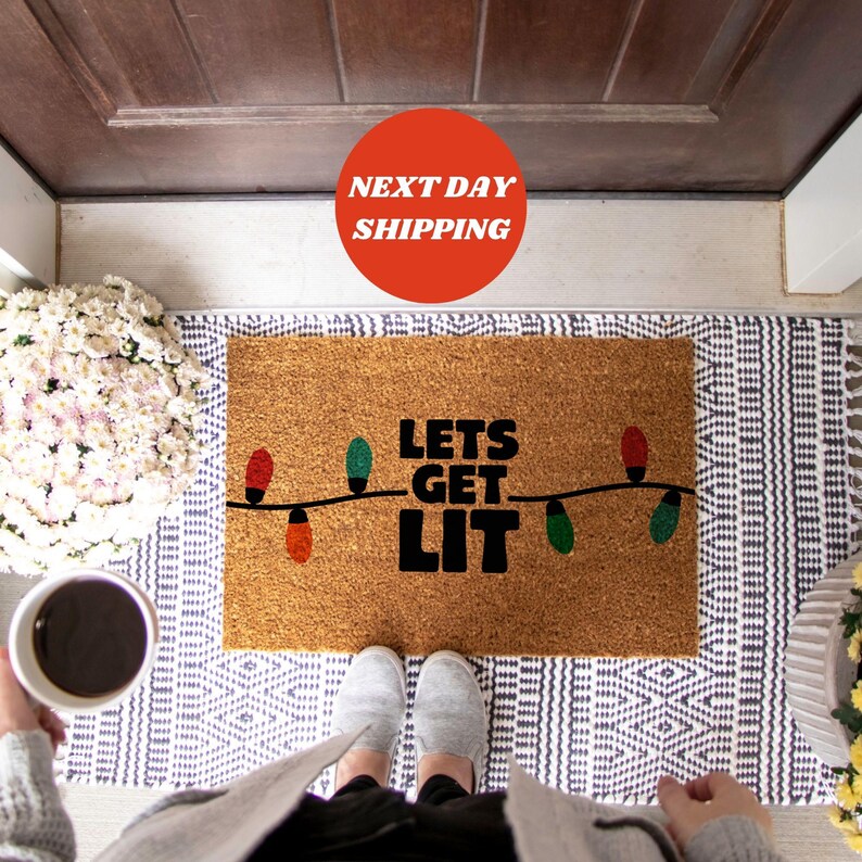 May include: A brown coir doormat with the text "Lets Get Lit" in black lettering. The text is surrounded by a string of colorful Christmas lights.