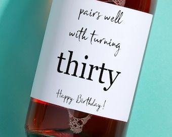 May include: A white wine bottle label with the text "pairs well with turning thirty Happy Birthday!" printed in black.