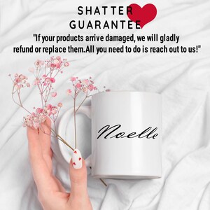 Puede incluir: Taza de cer&aacute;mica blanca con el nombre "Noelle" escrito en cursiva negra. La taza est&aacute; sobre una superficie blanca con flores rosas.