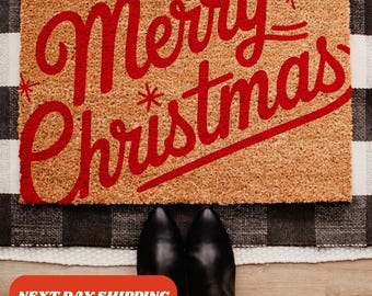 May include: A brown coir doormat with the text "Merry Christmas" in red cursive lettering. The text is decorated with small white stars.