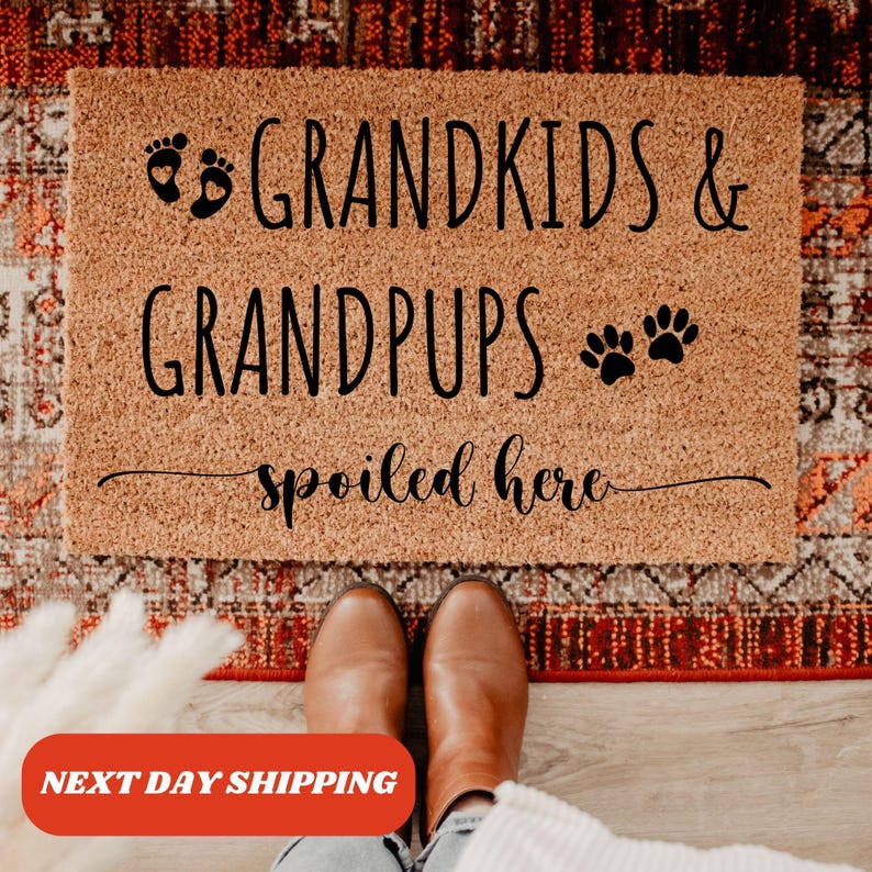 May include: A brown coir doormat with the text "Grandkids & Grandpups spoiled here" in black lettering. The text includes a footprint and paw print graphic.