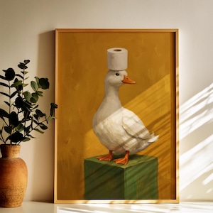 May include: A framed wall art print featuring a white duck with orange feet standing on a green cube. The duck has a roll of white toilet paper balanced on its head. The background is a solid mustard yellow color with visible brushstroke textures.