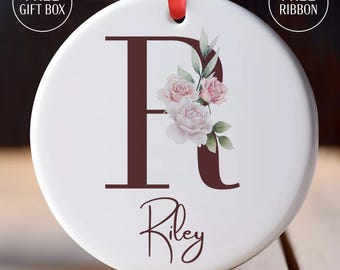 May include: White ceramic ornament with a brown letter R and pink watercolor flowers. The name Riley is written in cursive below the letter.