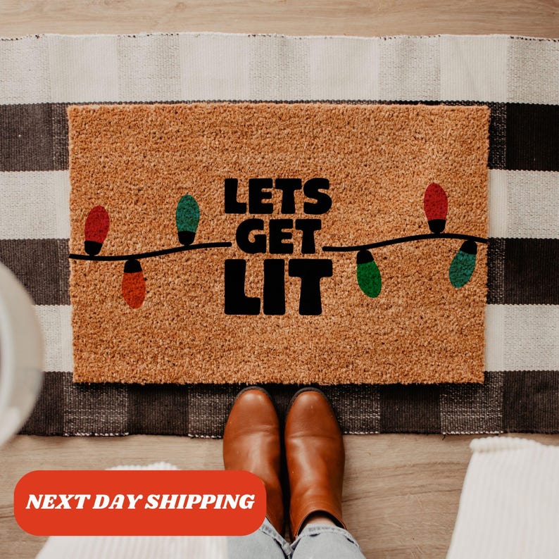 May include: A brown coir doormat with the text "Lets Get Lit" in black lettering. The text is surrounded by a string of colorful Christmas lights.