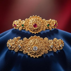 May include: Two ornate gold-colored hair clips. The top clip features a central red gemstone, flanked by green and red gems. The bottom clip has a central clear gemstone, with clear gems on either side. Both clips have floral and filigree designs.