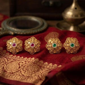 May include: Four gold-toned floral-shaped earrings featuring intricate filigree metalwork. Two earrings are centered with round pink stones, and two earrings are centered with round green stones, all surrounded by small clear accent stones.