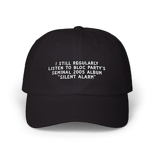 May include: Black baseball cap with a curved brim. The cap features white text that reads: "I STILL REGULARLY LISTEN TO BLOC PARTY'S SEMINAL 2005 ALBUM 'SILENT ALARM'". The cap is a classic, casual accessory.