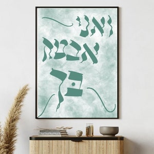 May include: A framed print with a teal blue watercolour background and Hebrew calligraphy in the same colour. The print is hanging on a white wall above a light brown cabinet with black legs. A woven chair is in the foreground.